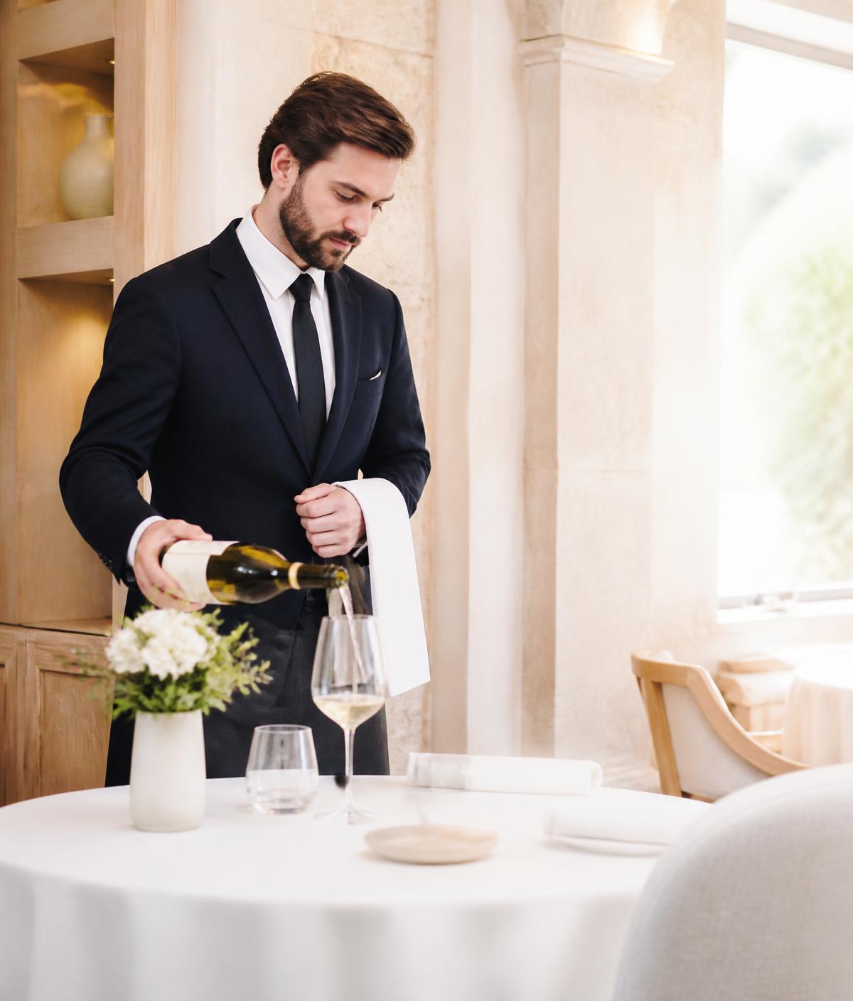 Sommelier pouring white wine at a sunlit table
