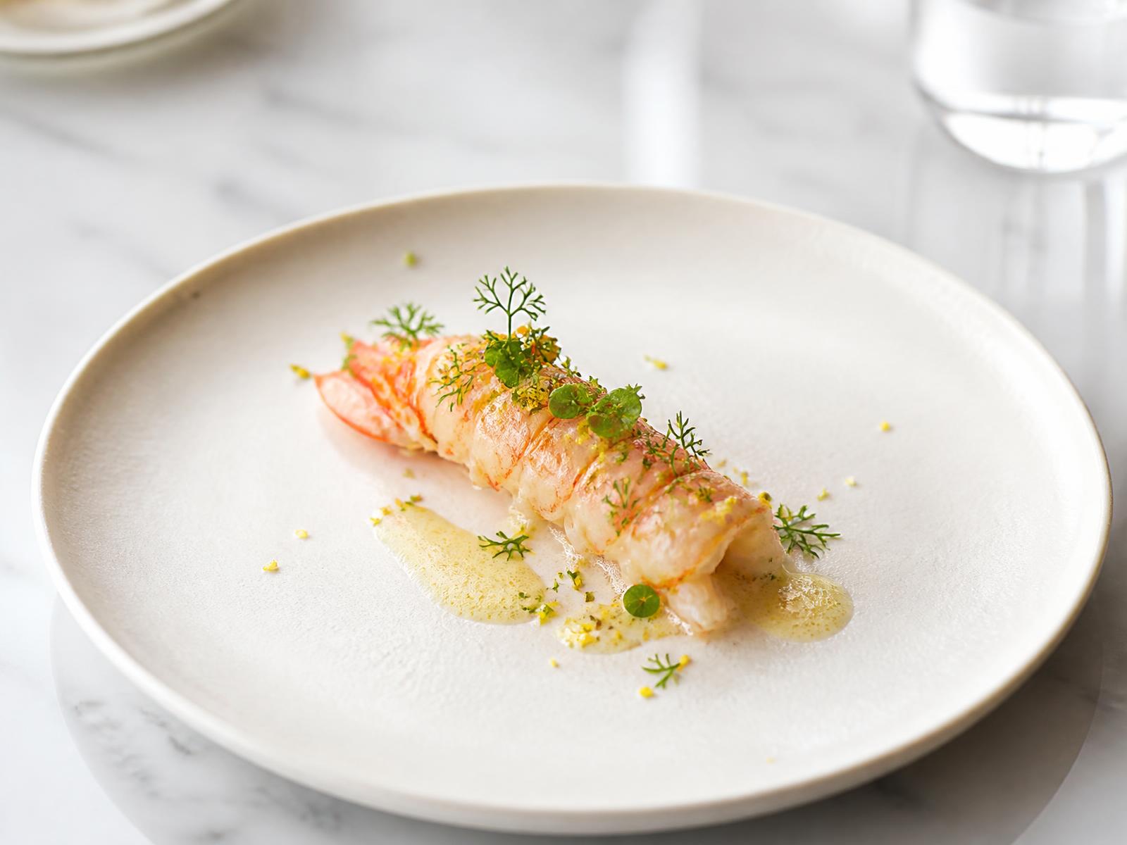 Langoustine tail with citrus emulsion, fennel pollen and micro herbs on ivory ceramic